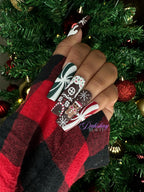 Hand with festive nail art in front of a decorated Christmas tree