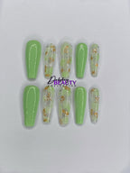 Set of green and clear nail extensions with gold accents on a white background.
