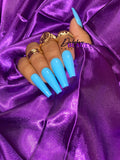 Hand with blue nails and gold rings on a purple satin background