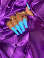 Hand with blue nails and gold rings on a purple satin background