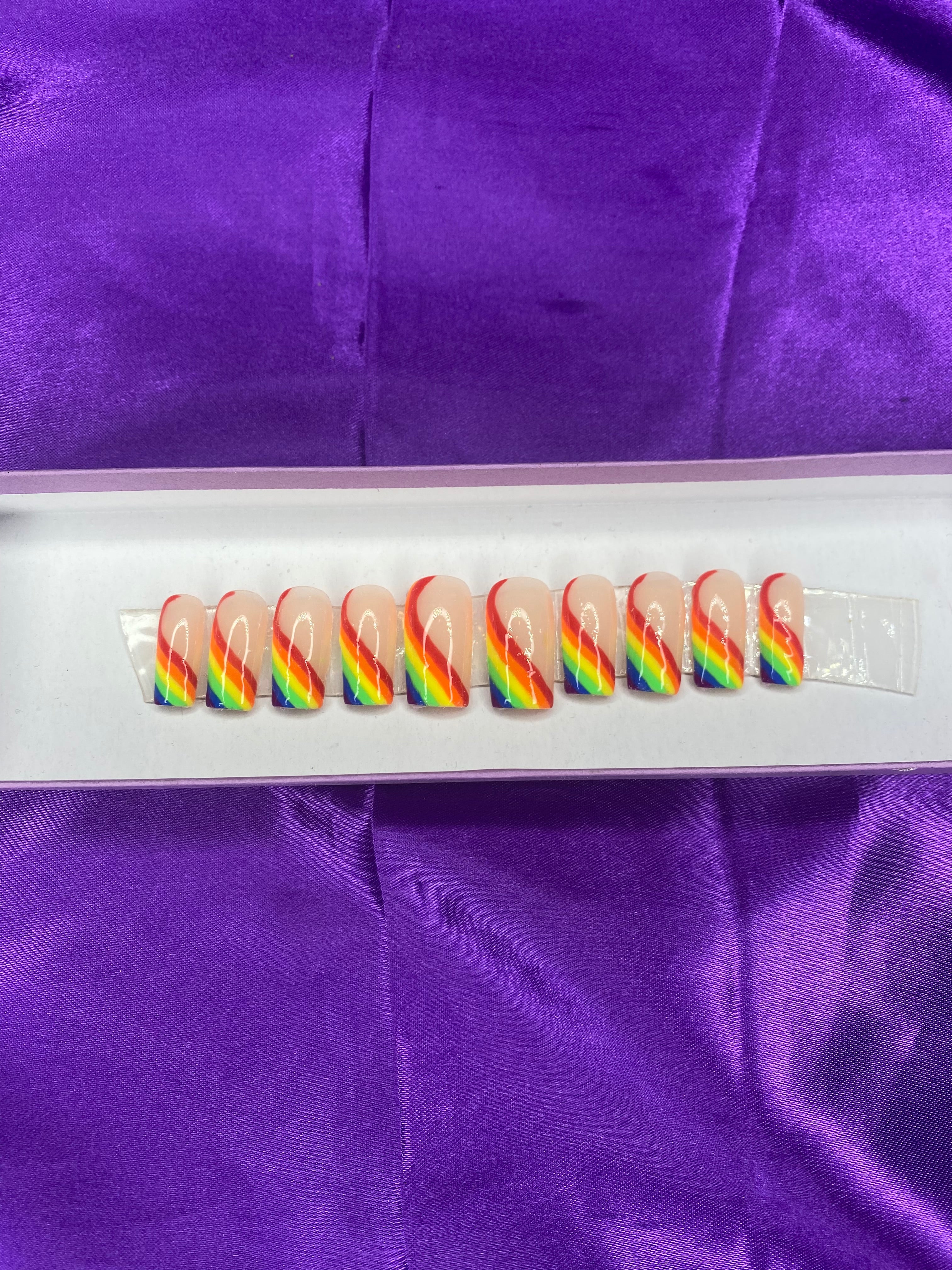 Set of colorful nail art designs on a white card with purple fabric background