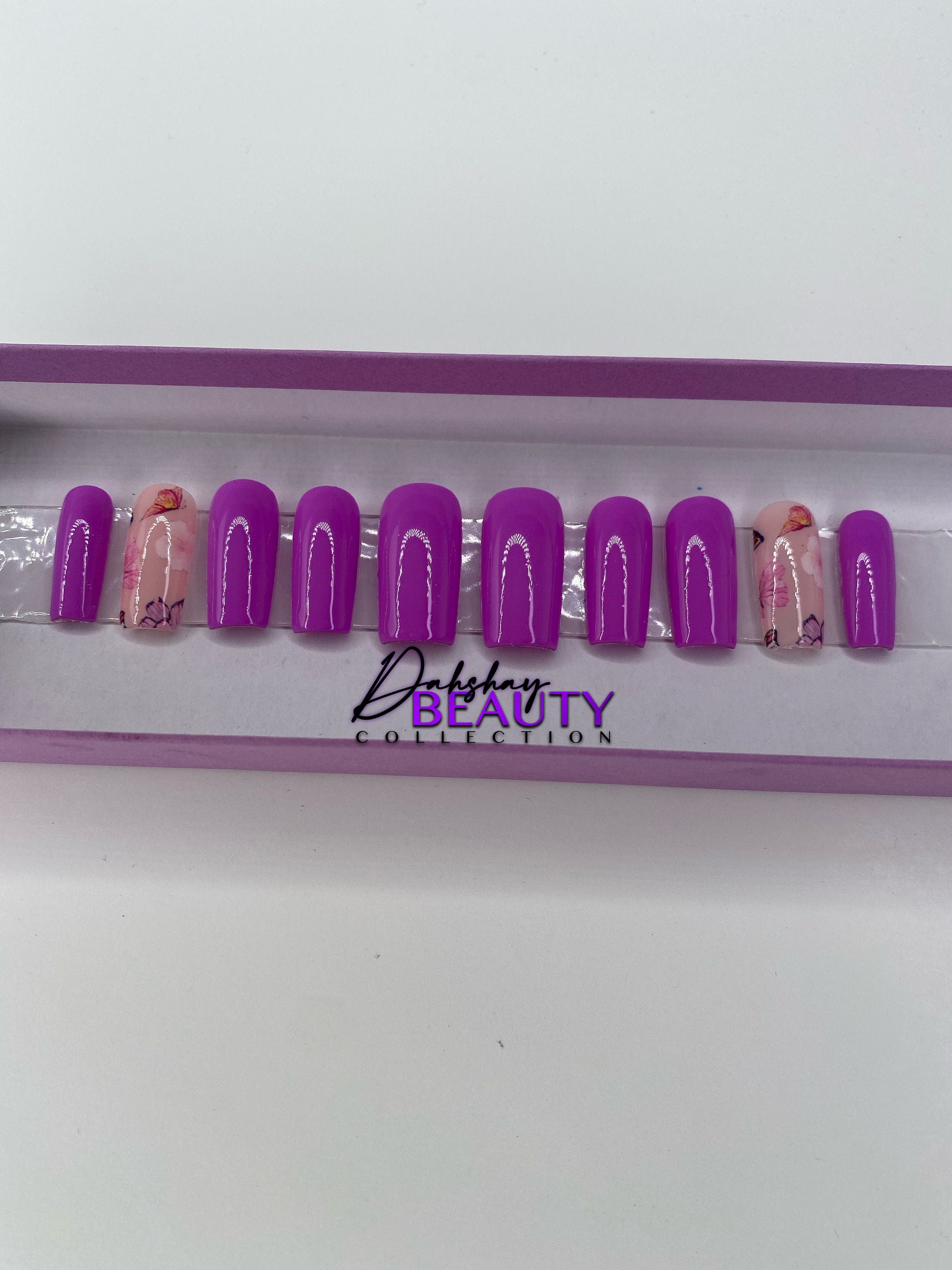 Purple press on nails with a floral design in a display case.