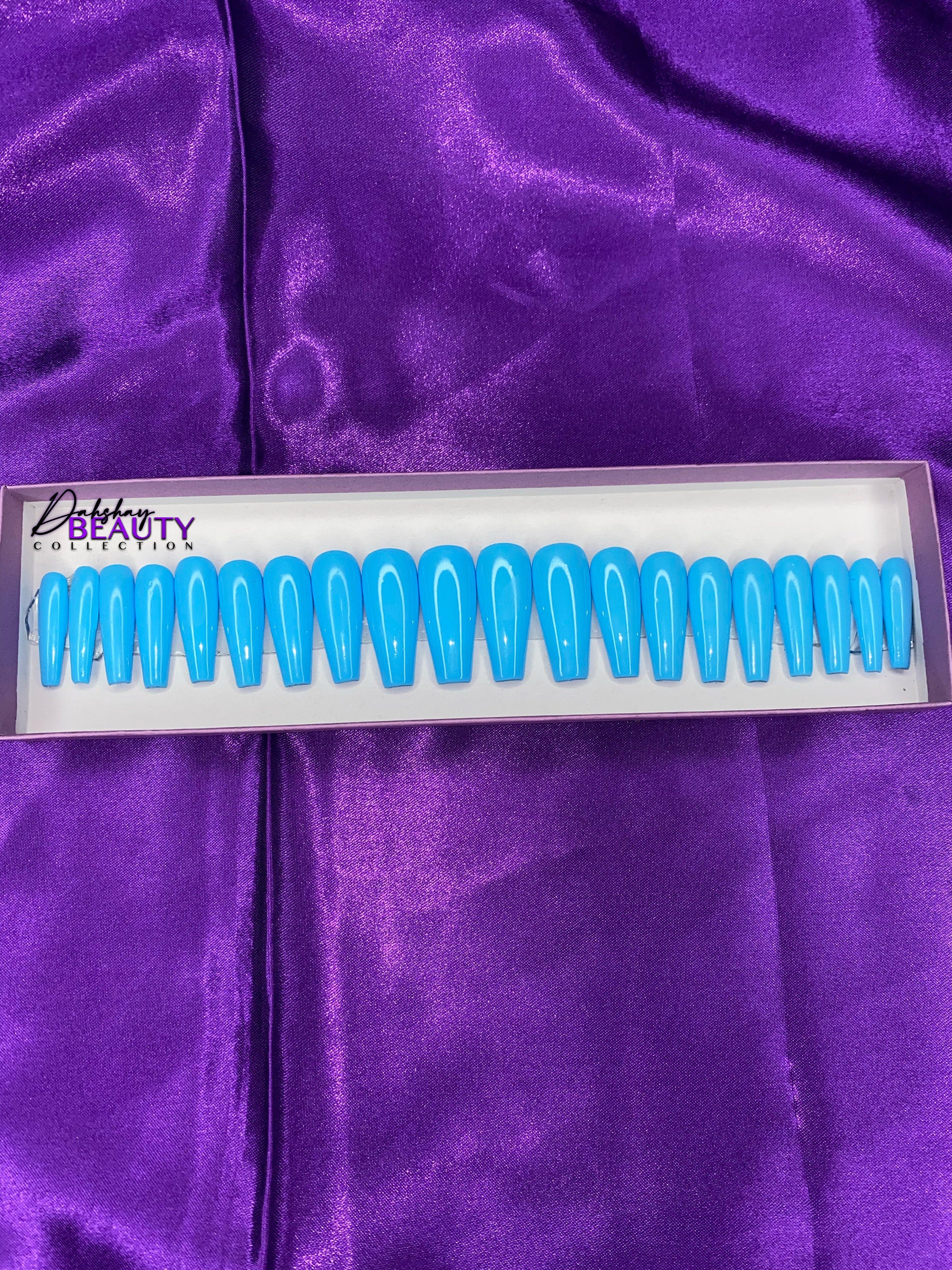 Set of blue false nails in a white and light purple box on a purple fabric background