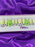 Set of decorative false nails with cow print and green accents on a purple fabric background