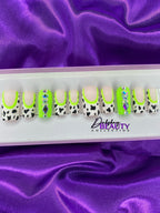 Set of decorative false nails with cow print and green accents on a purple fabric background