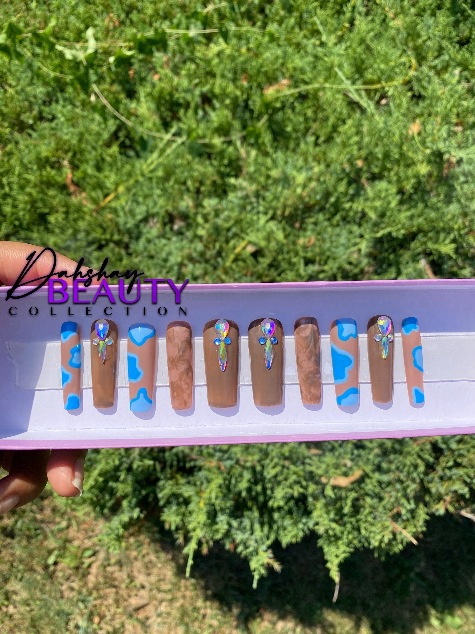 Nail art display with blue and brown designs held against a green outdoor background