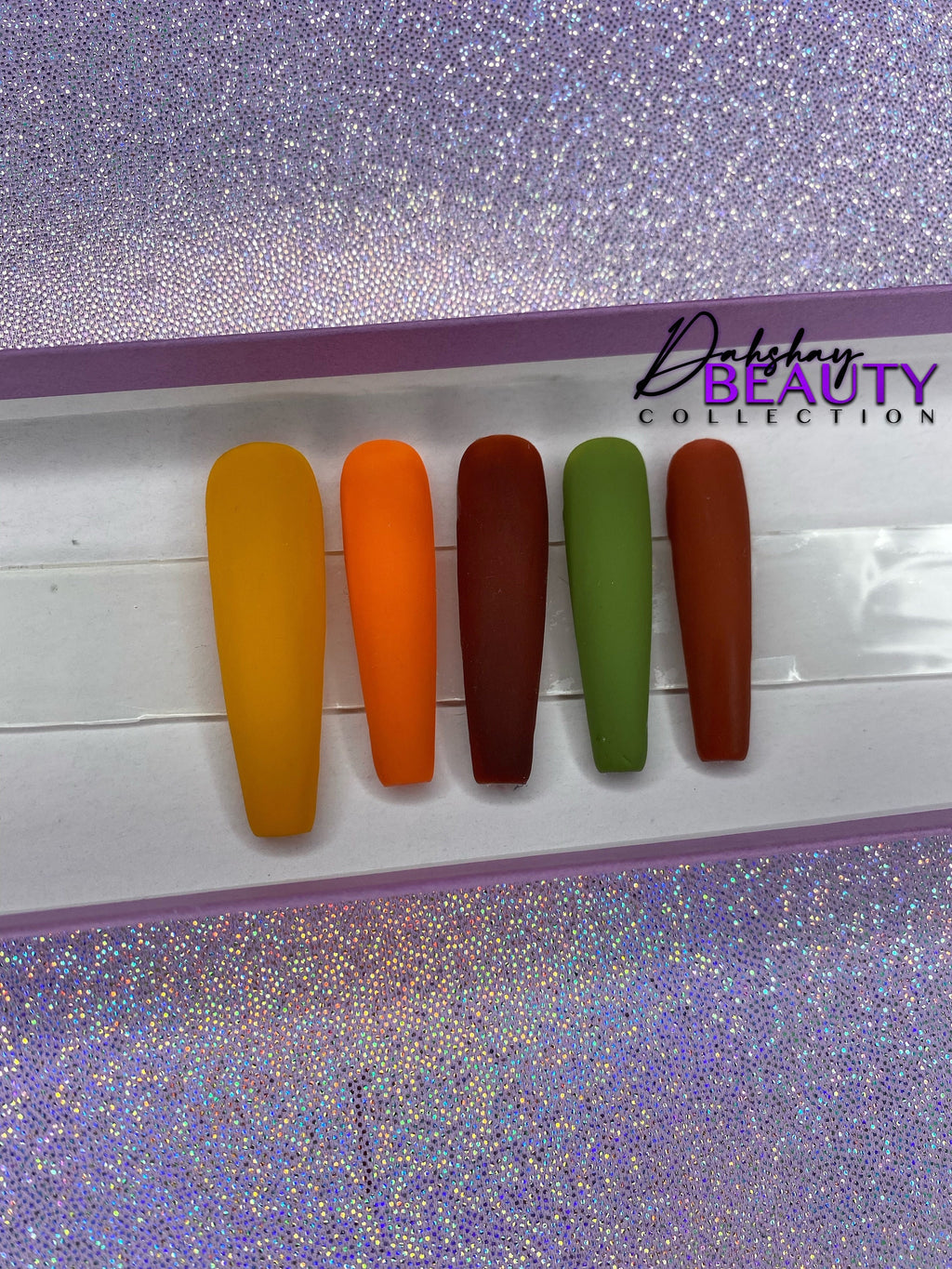 Set of false nails in various Fall colors on a display card with a purple glitter background.