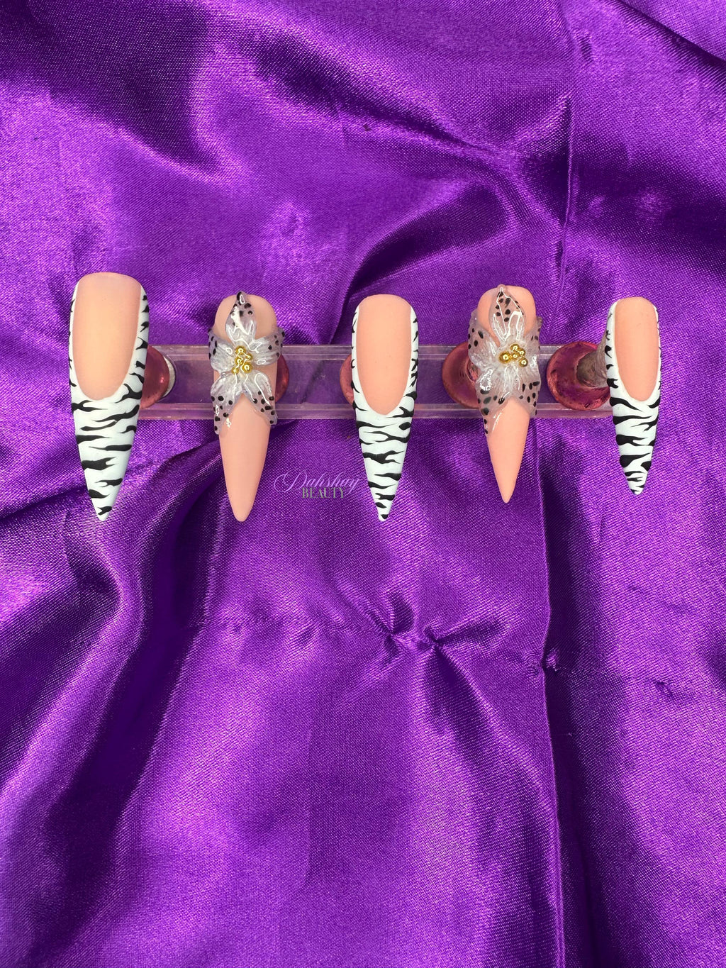 Set of decorative false nails with zebra pattern and a blue flower with black dots on the edge on a purple satin background
