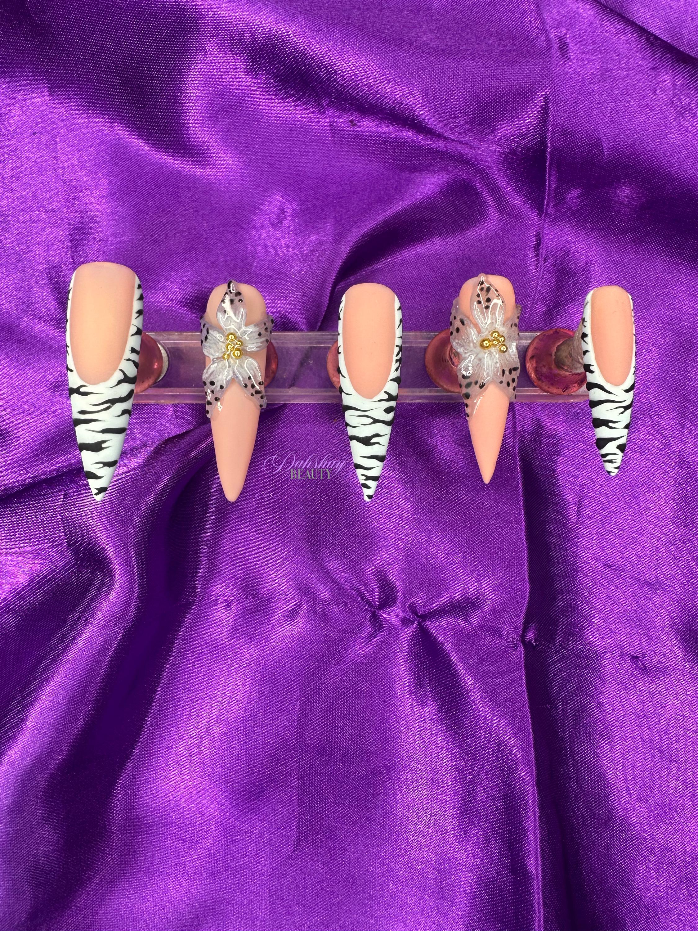 Set of decorative false nails with zebra pattern and a blue flower with black dots on the edge on a purple satin background