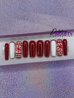 Set of red and white Christmas nail extensions with red glitter and a snowflake design on a purple glittery background.