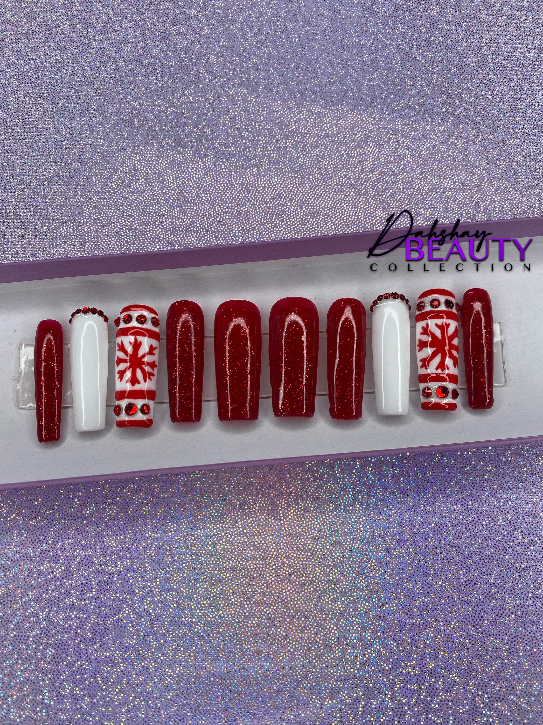 Set of red and white Christmas nail extensions with red glitter and a snowflake design on a purple glittery background.