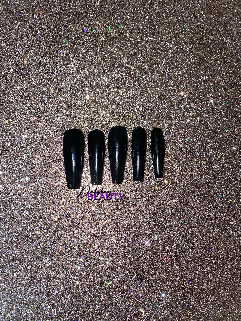 Set of black false nails on a glittery gold background.