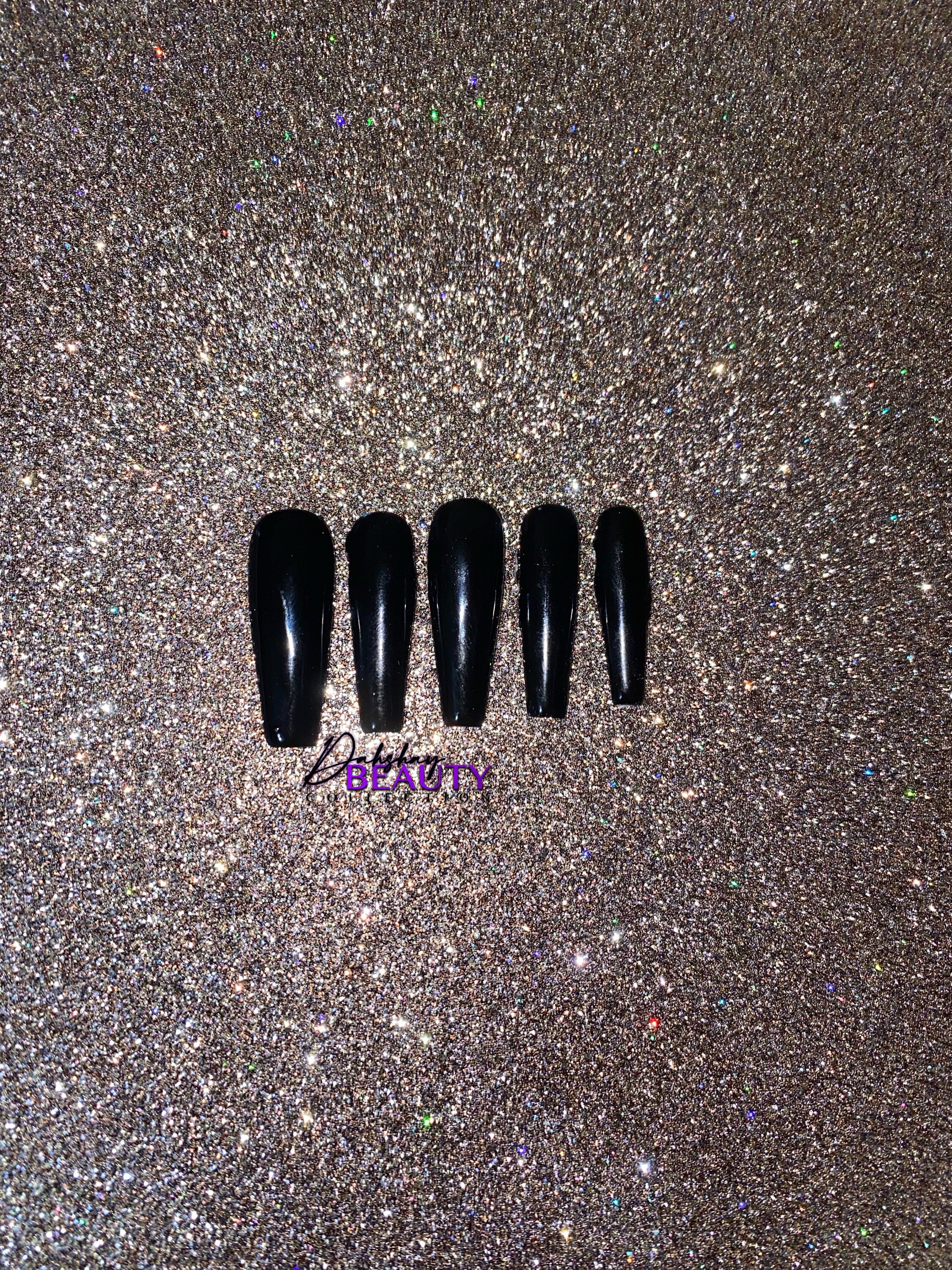 Set of black false nails on a glittery gold background.