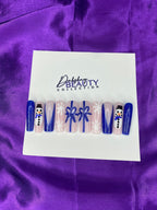 Press On Nails with Christmas designs of snowmen, bows  and a snowflake on a white card against a purple satin background.