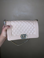Nude quilted handbag with chain detail held by a hand against a plain background
