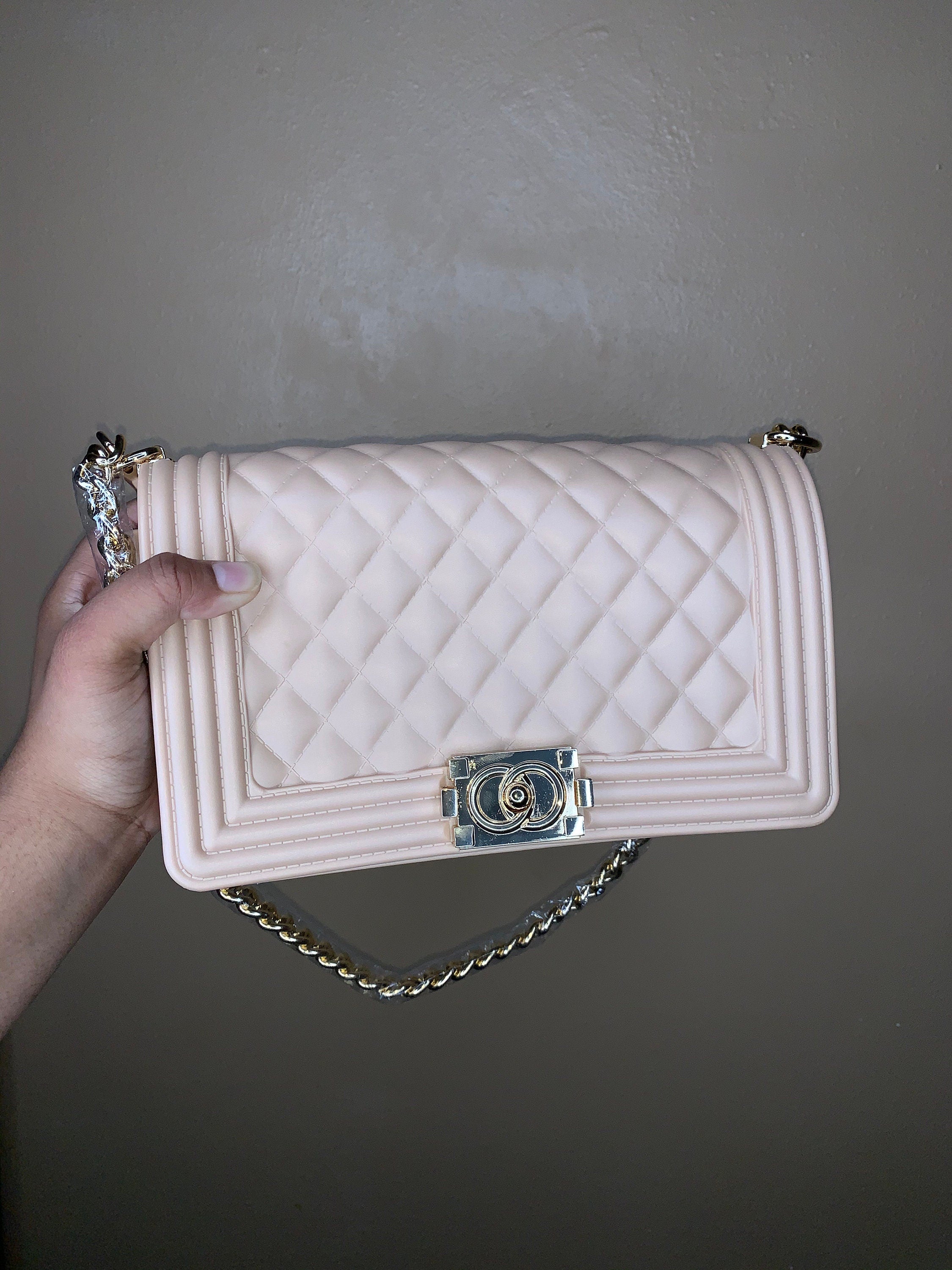 Nude quilted handbag with chain detail held by a hand against a plain background