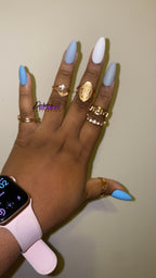 Hand with blue, grey and white nails wearing gold rings and a smartwatch on a plain background