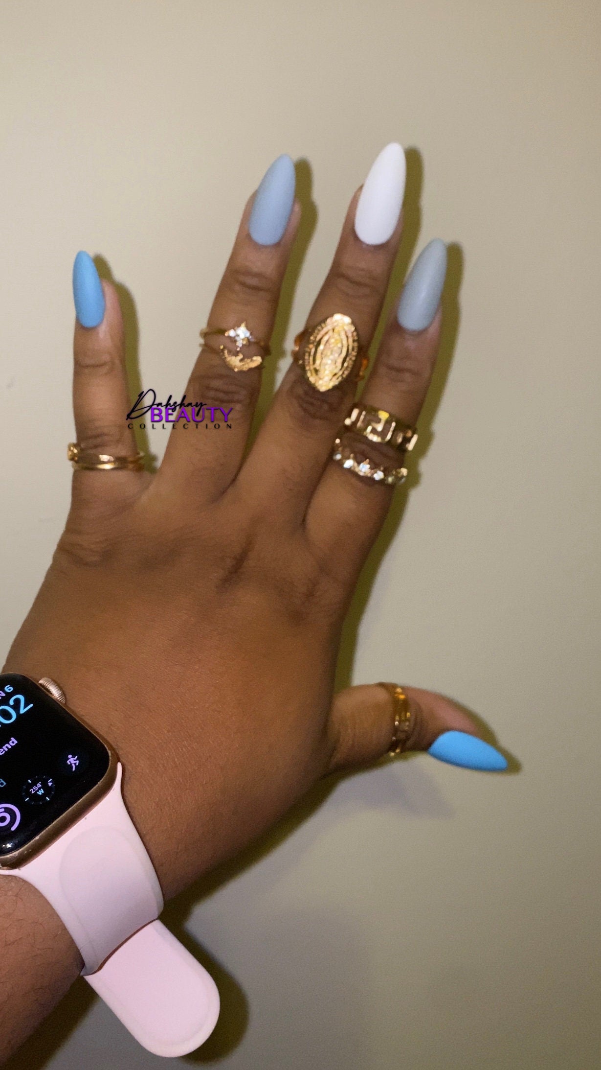 Hand with blue, grey and white nails wearing gold rings and a smartwatch on a plain background