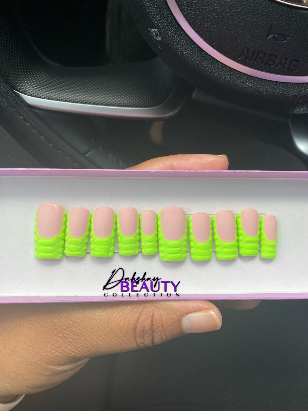 Display of false nails with green nails with 3D stripes held by a hand, against a car interior background.