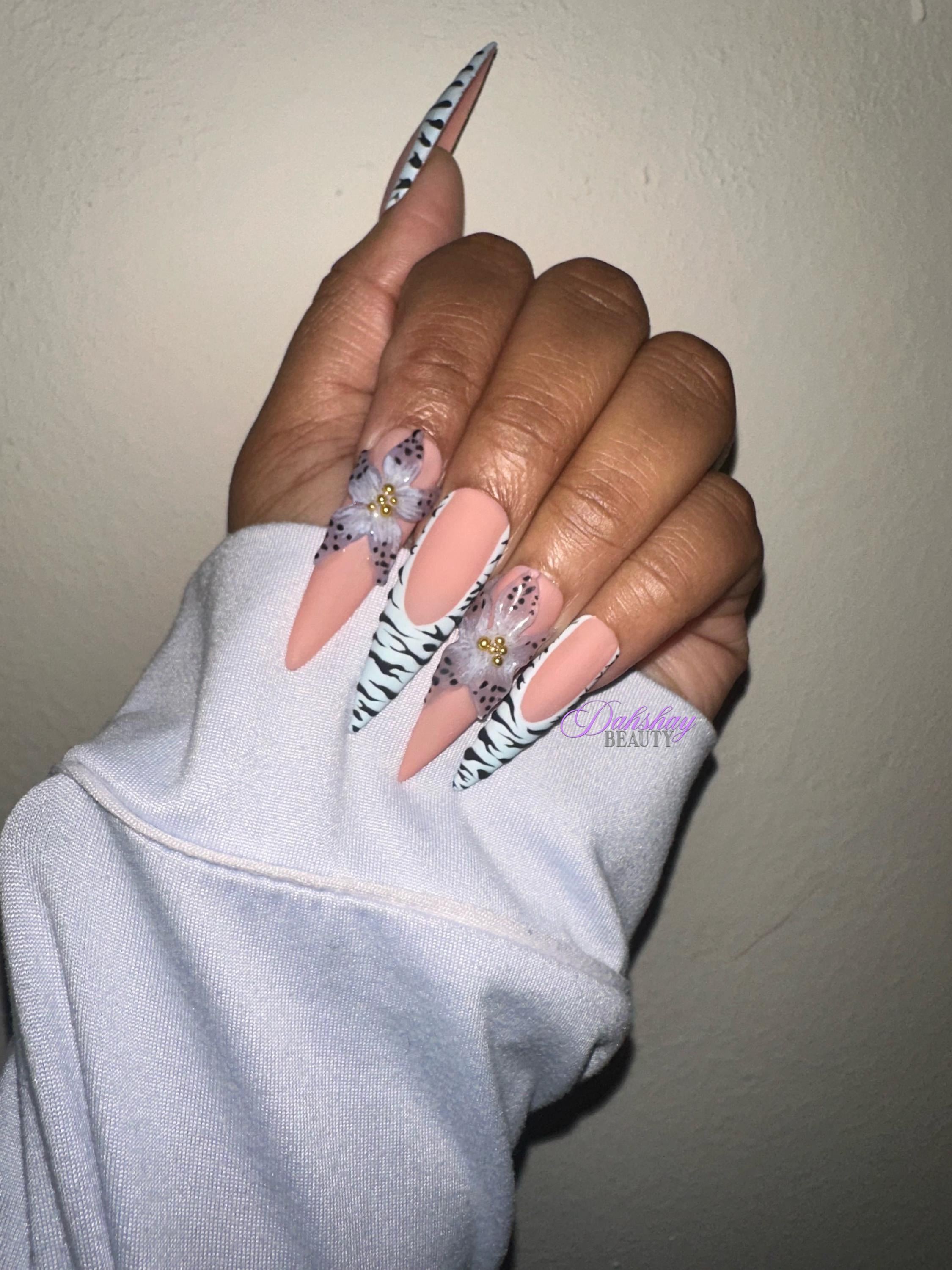 Hand with floral nail design wearing a light blue sleeve against a beige background with gold rings