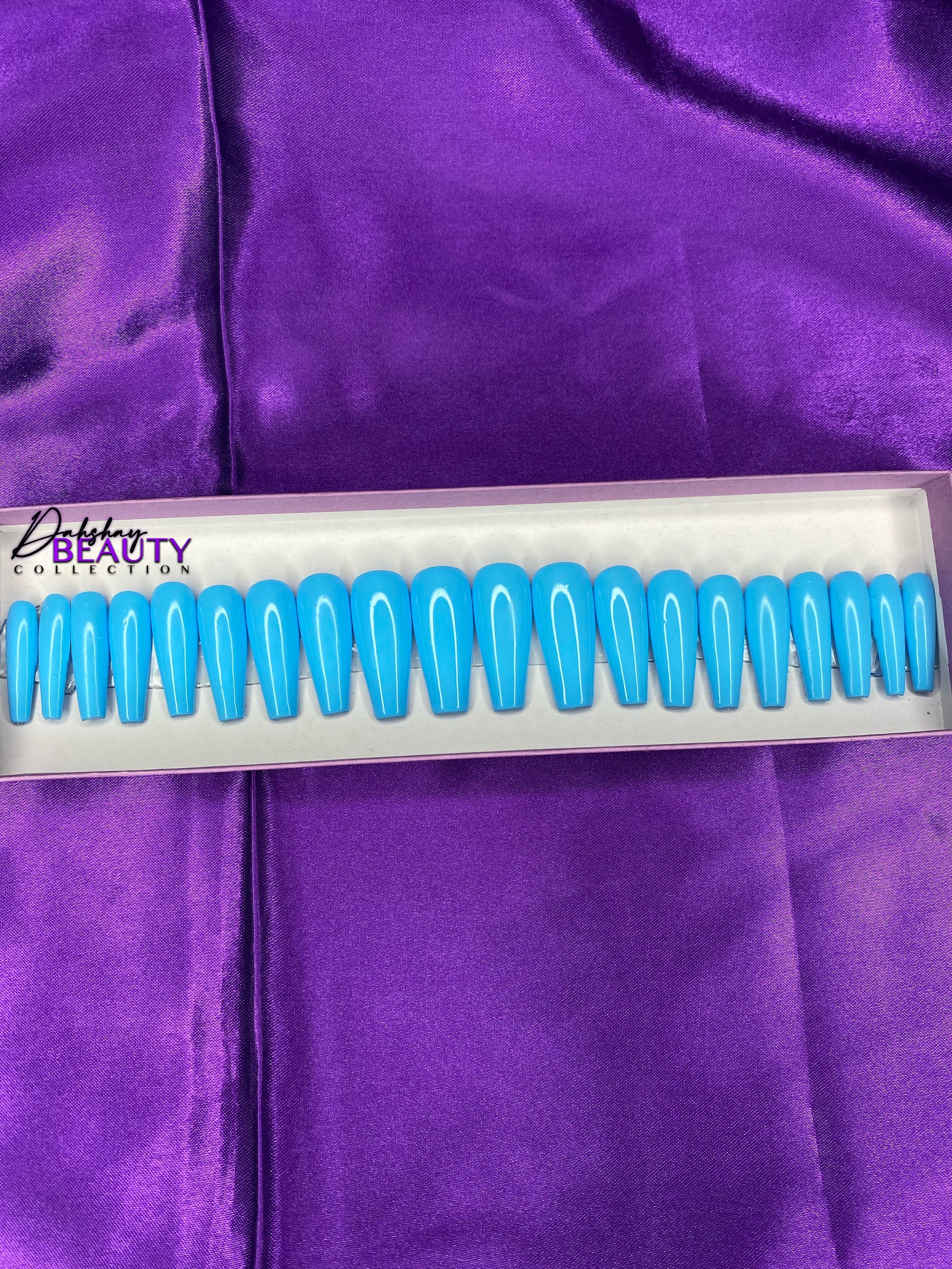 Set of blue false nails in a white and light purple box on a purple fabric background