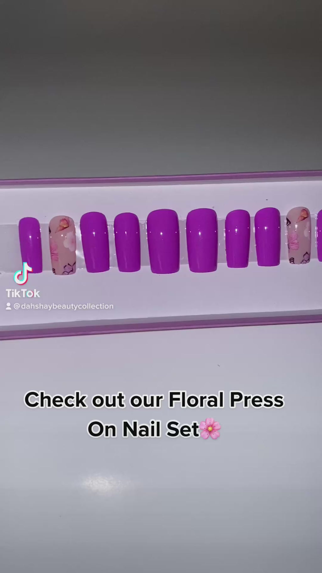 A video of purple press on nails with a floral design in a display case.