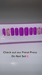 A video of purple press on nails with a floral design in a display case.