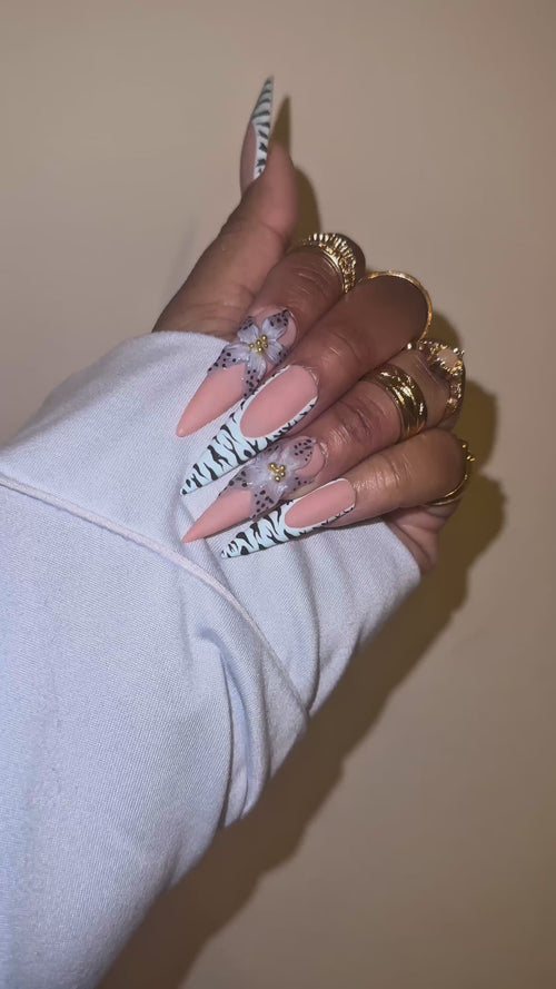 A video of a set of decorative false nails with zebra pattern and a blue flower with black dots on the edge with a beige background