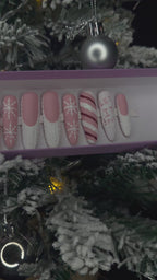 A video of a set of Christmas false nails with snowflakes, candy cane and sweater designs in front of a Christmas tree.
