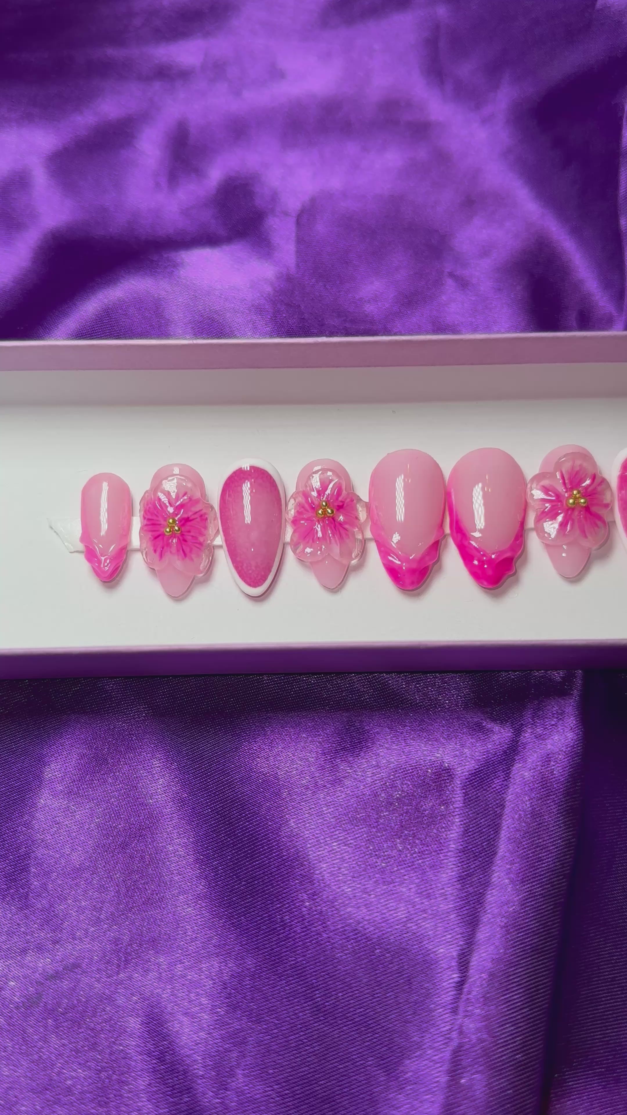 A video of a set of pink floral press on nails on a purple satin background