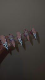 A video of a set of decorative false nails with zebra pattern and a blue flower with black dots on the edge with a beige background