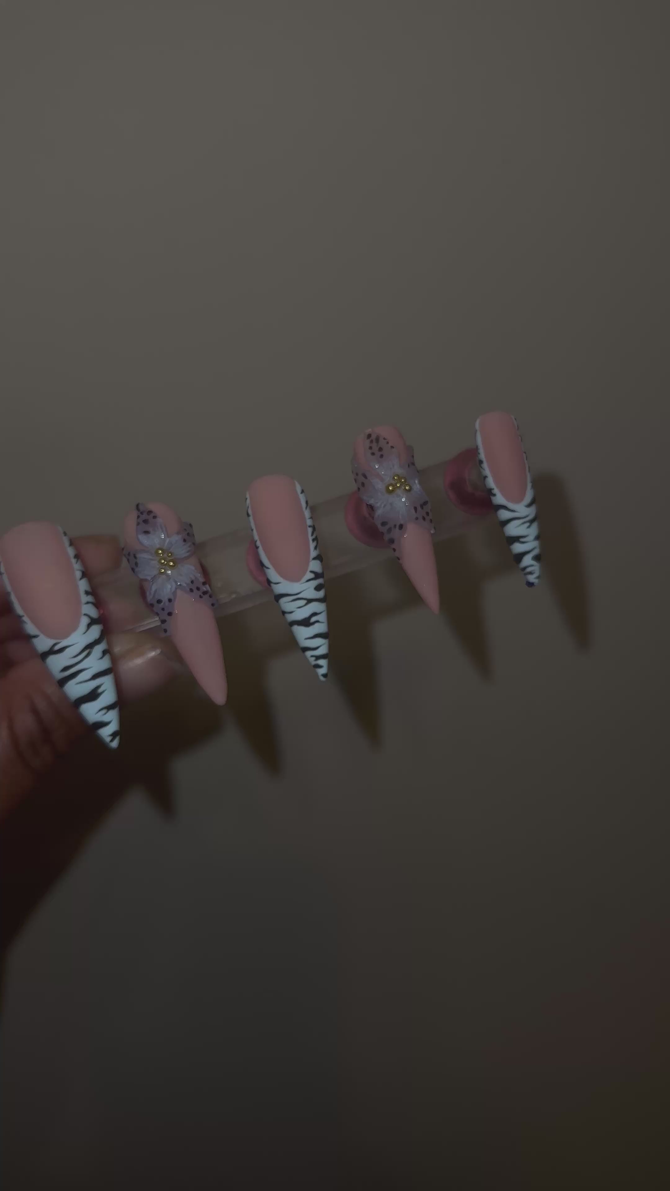 A video of a set of decorative false nails with zebra pattern and a blue flower with black dots on the edge with a beige background