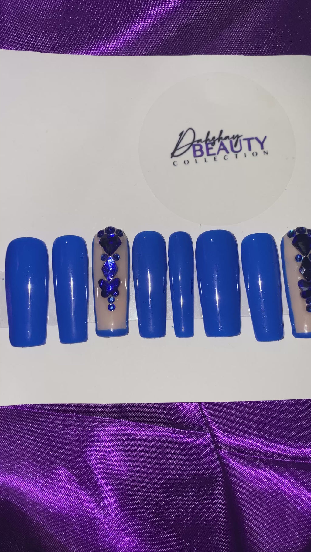 A video of Blue nails with a rhinestone design on a purple satin background