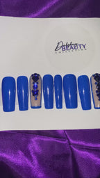 A video of Blue nails with a rhinestone design on a purple satin background