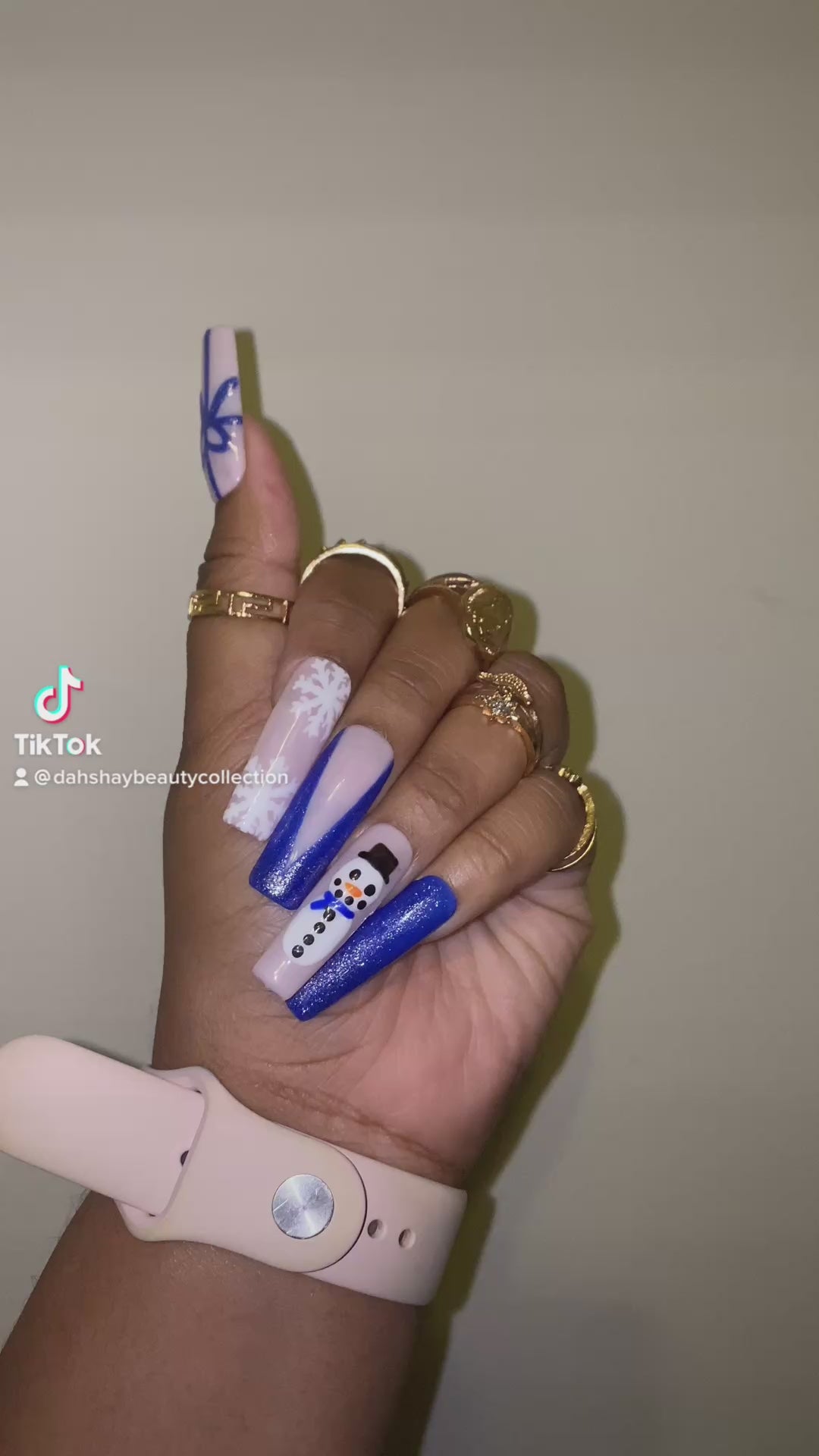 A video of press on nails with Christmas designs of snowmen, bows  and a snowflake on a hand with a plain background.