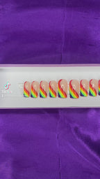 A video of rainbow-colored press-on nails on a white tray against a purple satin background.