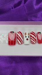 A video of a set of Christmas nails with a reindeer, candy cane and french tip design on a purple satin background.