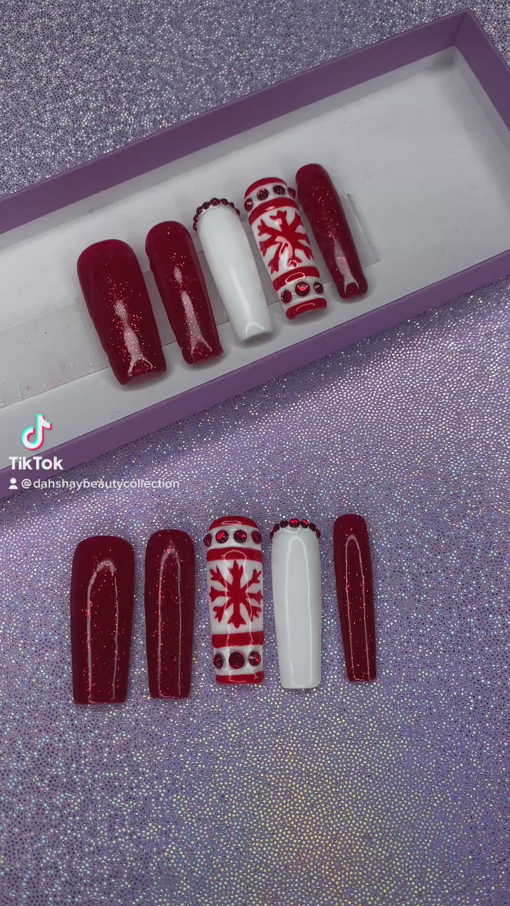A video of a set of red and white Christmas nail extensions with red glitter and a snowflake design on a purple glittery background.