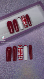 A video of a set of red and white Christmas nail extensions with red glitter and a snowflake design on a purple glittery background.