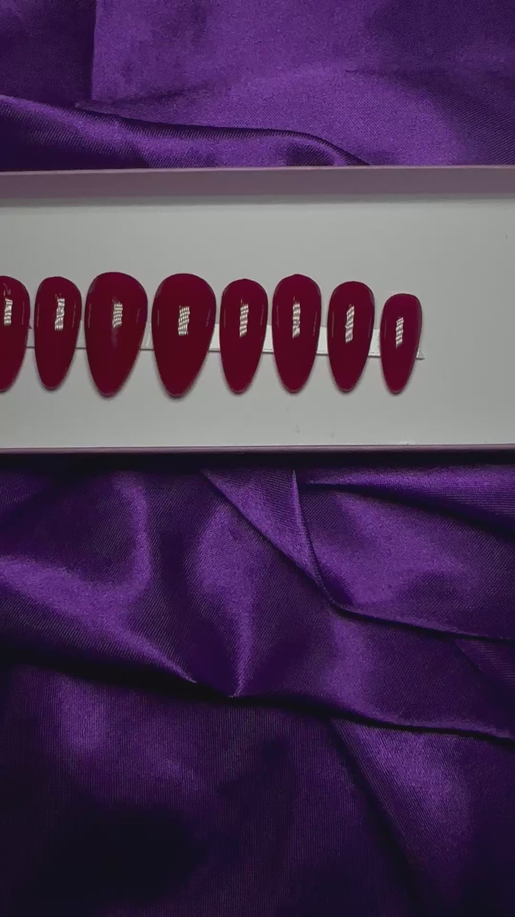 A video of a set of red press on nails on a purple satin background