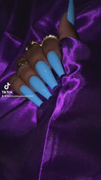 Video of hand with blue nails and gold rings on a purple satin background