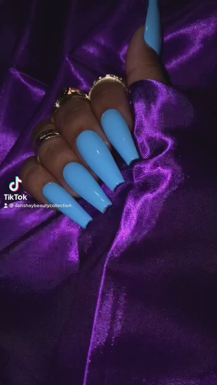 Video of hand with blue nails and gold rings on a purple satin background